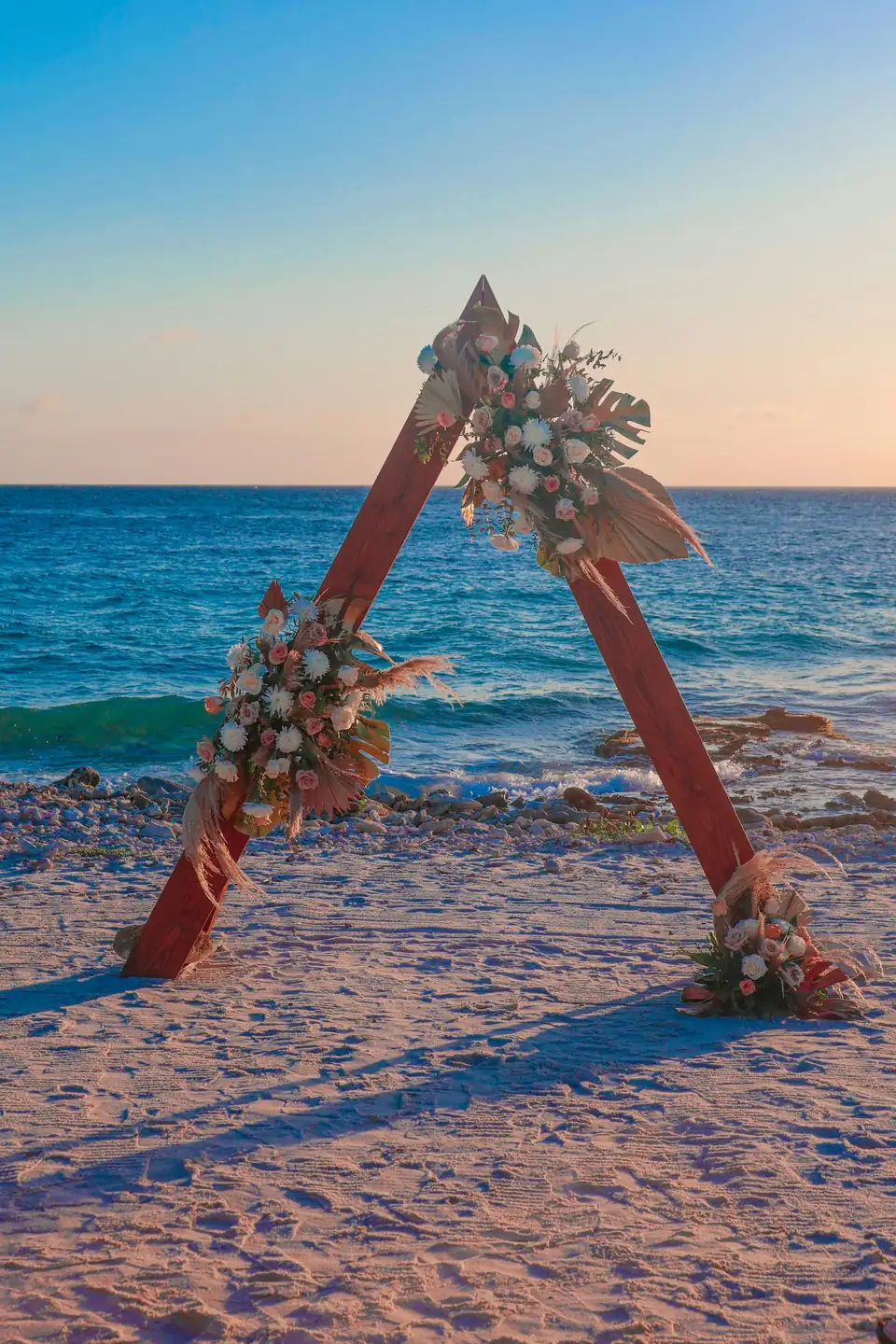 Arco de madera con flores en la orilla del mar al atardecer