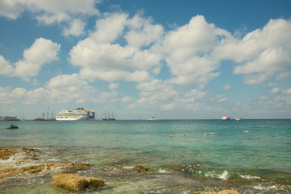 Crucero anclado a lo lejos frente a una costa rocosa de aguas turquesa en el Caribe