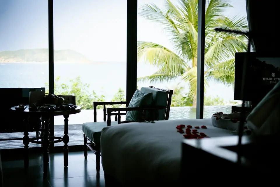 Habitación de hotel con ventanales y vista al mar entre palmeras