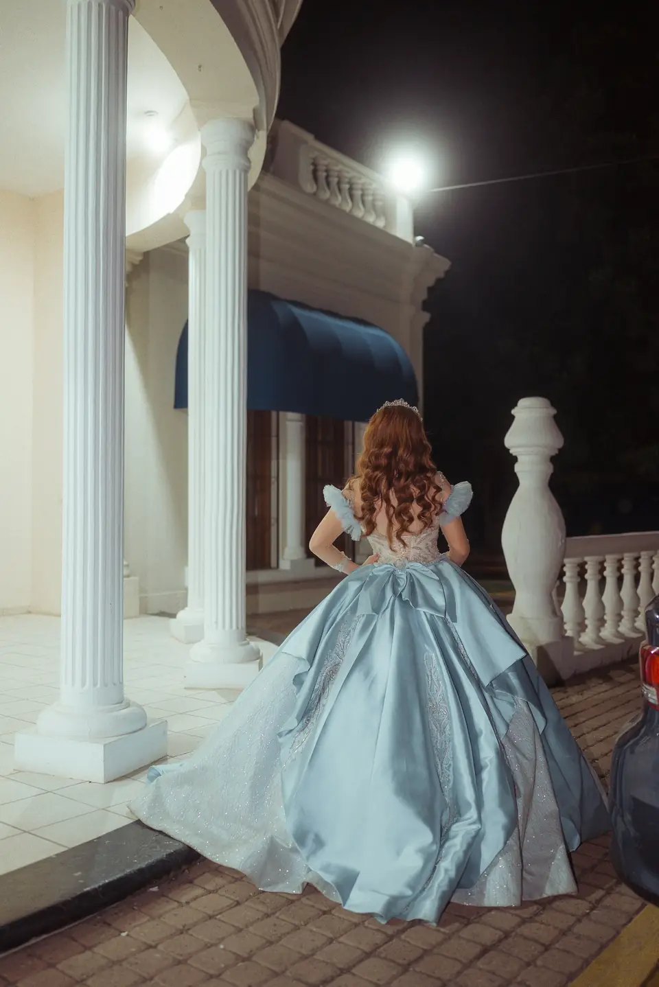 Quinceañera de vestido azul claro vista de espaldas en una terraza iluminada