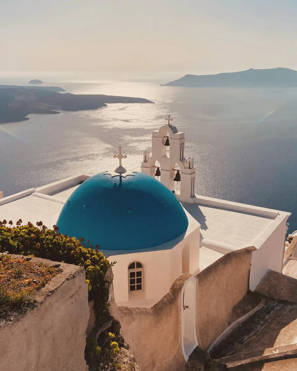 Iglesia de cúpula azul y campanario blanco frente al mar Egeo en Santorini, Grecia
