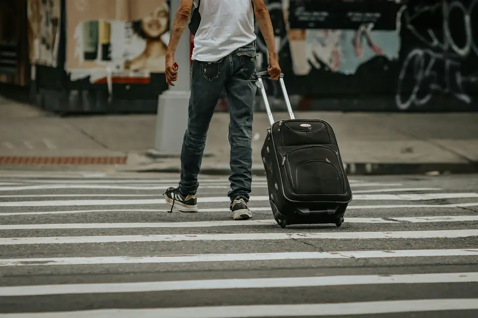 Viajero cruzando la calle con su maleta de ruedas